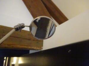 Inspectie van schilderwerk op een kozijn. In de spiegel is een hechtingsgebrek zichtbaar.